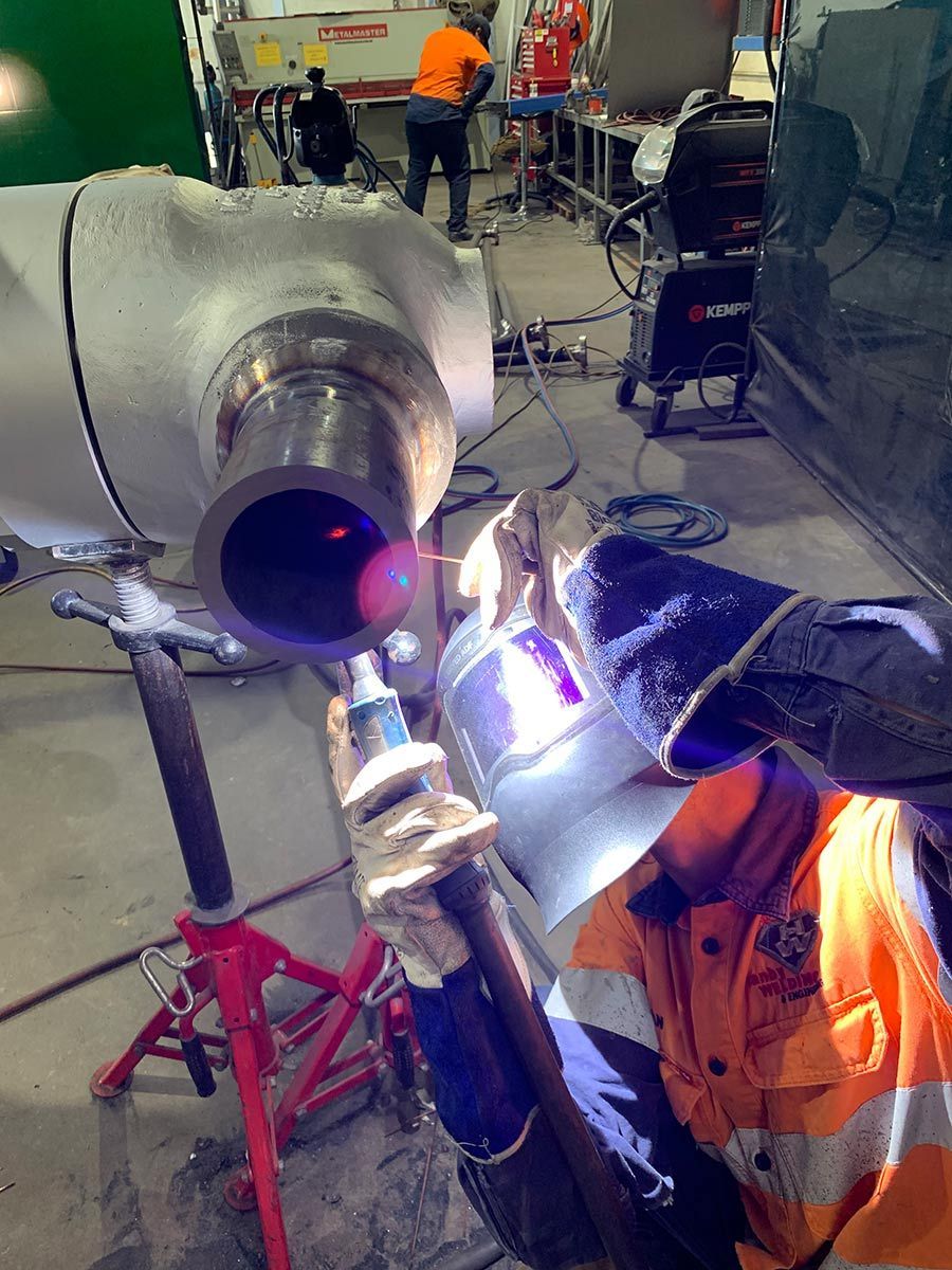 A Man Is Welding A Pipe In A Factory — Hanby Welding & Engineering In Portsmith, QLD
