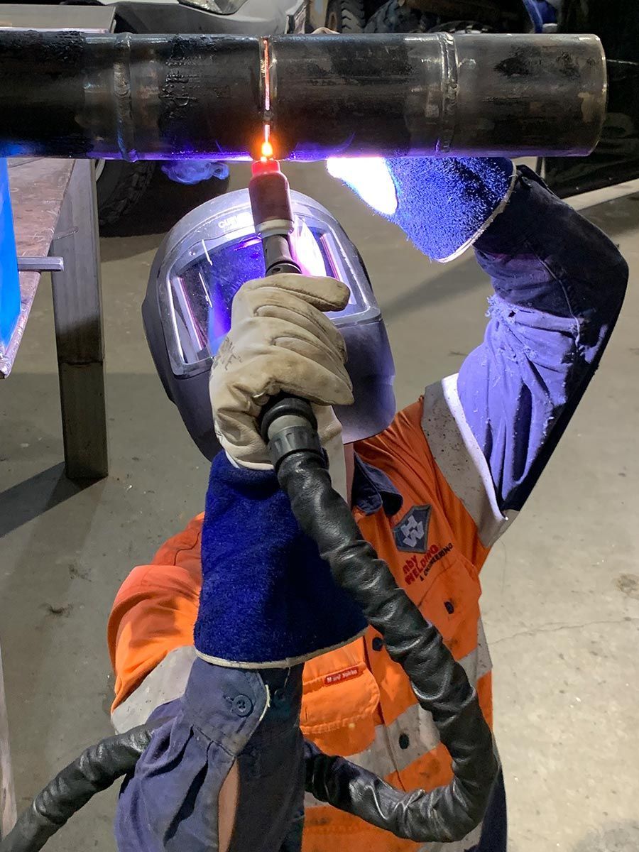 A Man Wearing A Welding Helmet Is Welding A Pipe — Hanby Welding & Engineering In Portsmith, QLD
