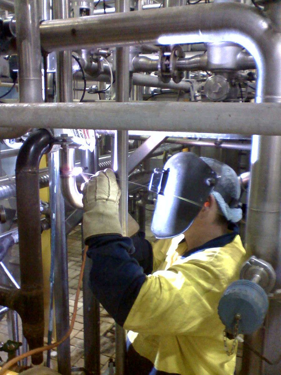 A Man Wearing A Welding Mask Is Working On Pipes — Hanby Welding & Engineering In Portsmith, QLD