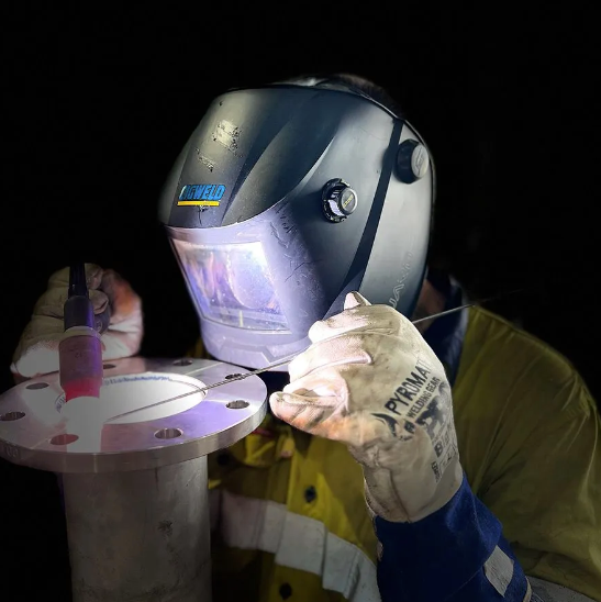 Welder in protective gear using a torch on a metal flange.