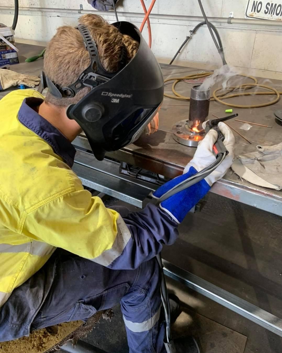 A Man Wearing A Welding Mask Is Welding A Piece Of Metal — Hanby Welding & Engineering In Portsmith, QLD