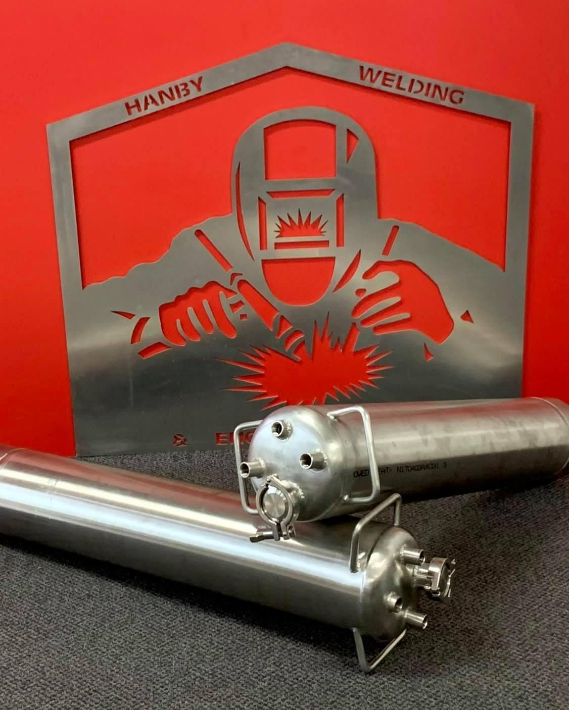 Two Stainless Steel Cylinders Are Sitting In Front Of A Welding Sign — Hanby Welding & Engineering In Portsmith, QLD