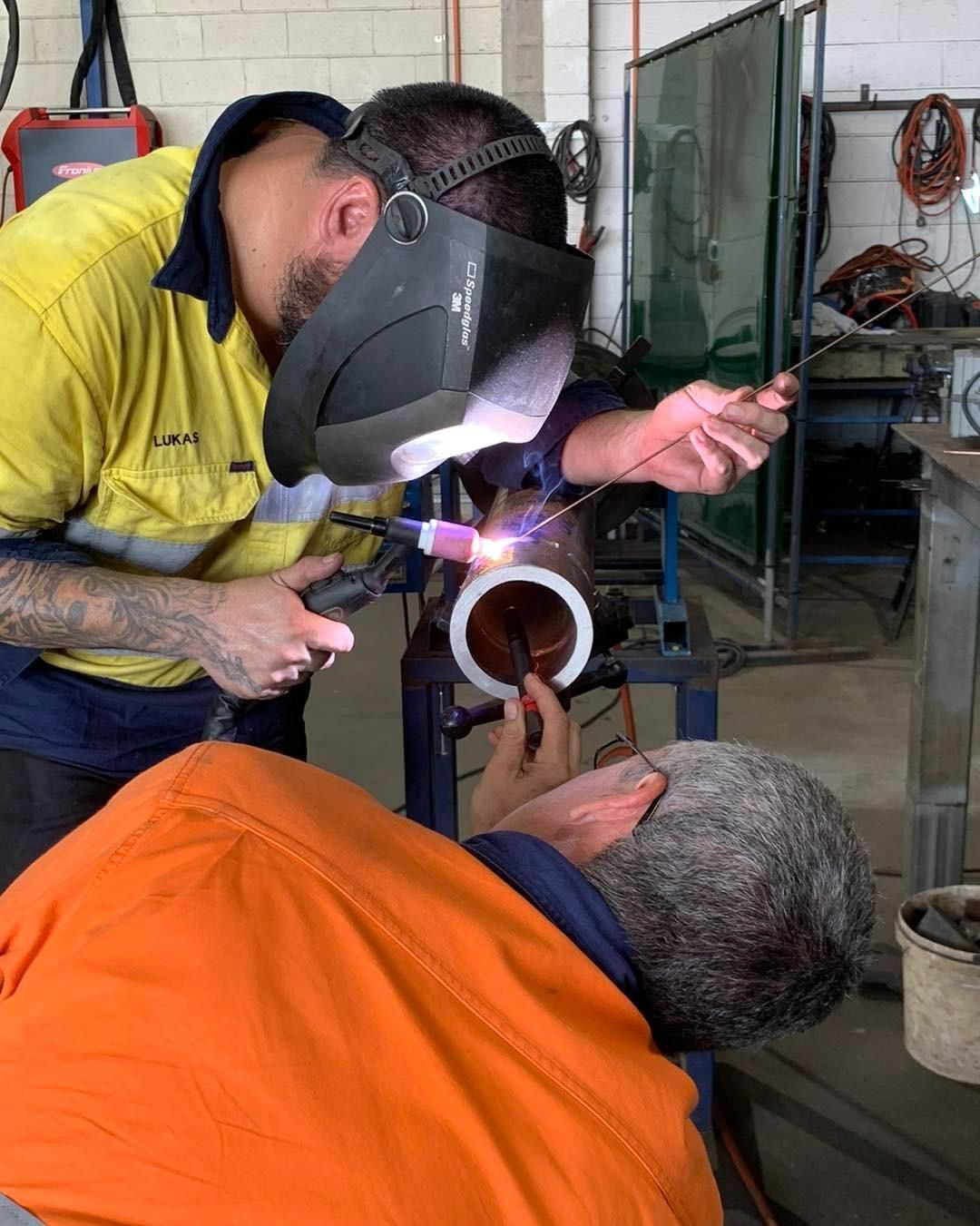 Two Men Are Welding A Pipe Together In A Factory — Hanby Welding & Engineering In Portsmith, QLD