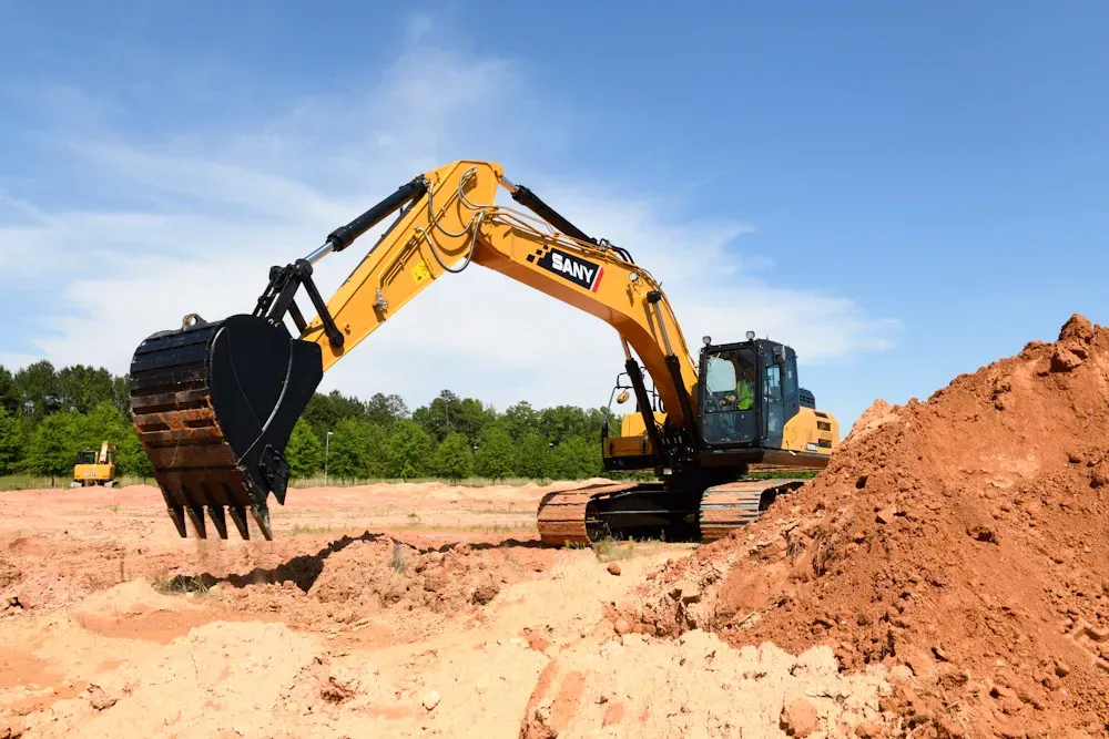 Yellow excavator digging in a dirt field under a blue sky.