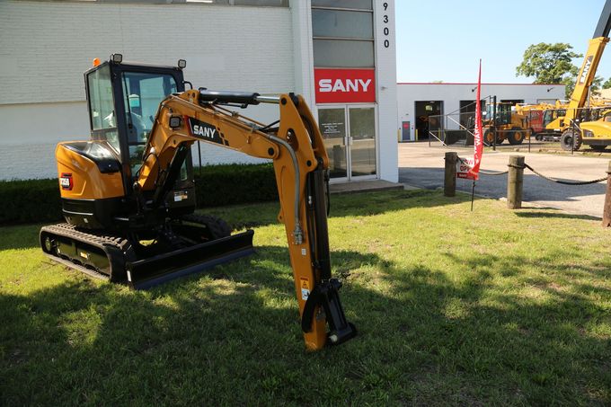 Yellow SANY excavator on green grass in front of a building.