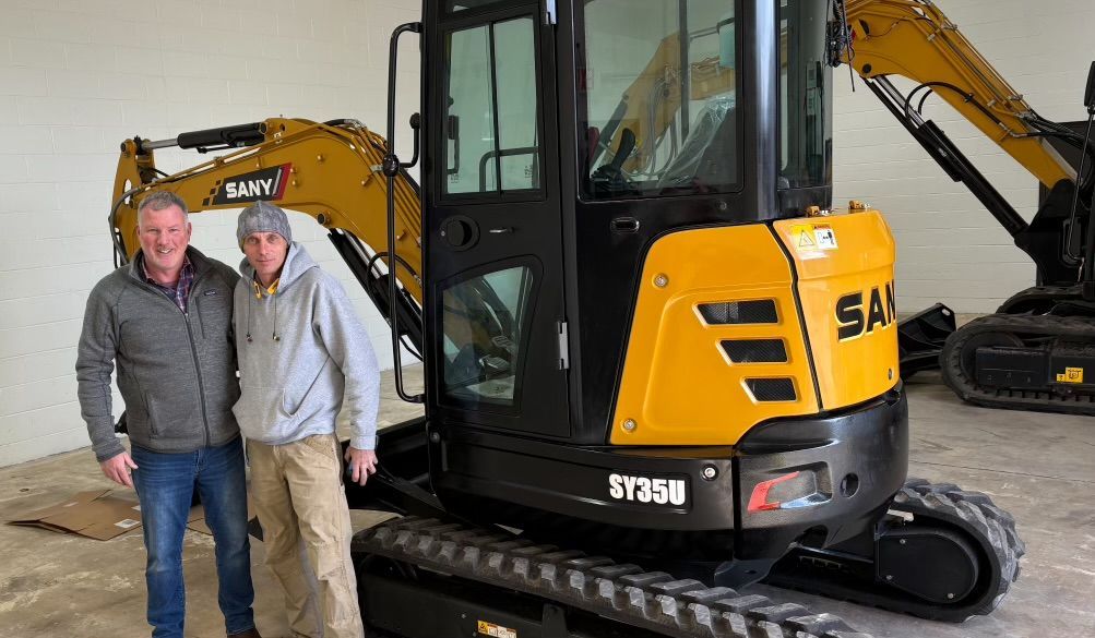 Two men standing beside a yellow and black SANY SY35B mini excavator.