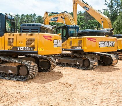 Yellow Sany excavators parked on a dirt surface with trees in the background.