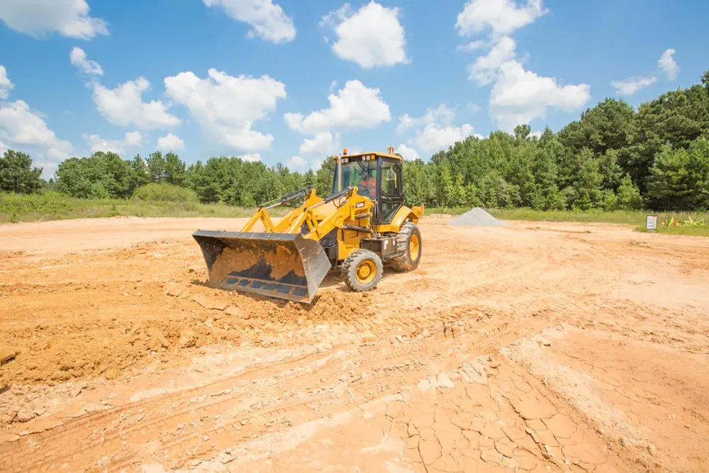 Yellow bulldozer on a construction site, moving dirt under a blue, cloudy sky.