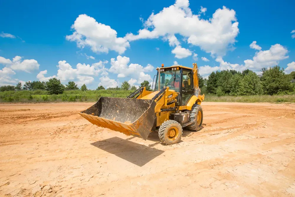 Yellow loader on a dirt lot under a blue sky, with trees in the background.