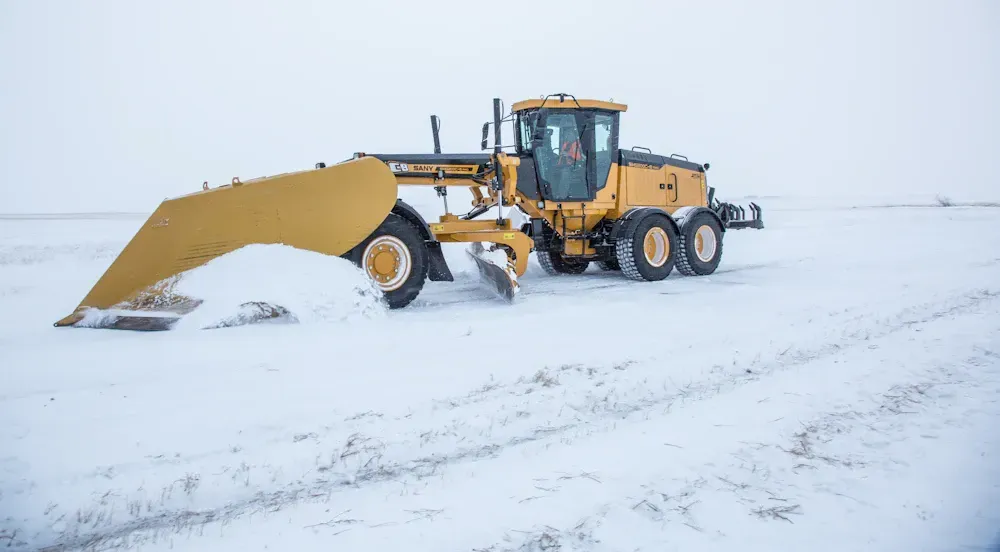 Yellow grader plowing snow on a flat, snowy landscape.