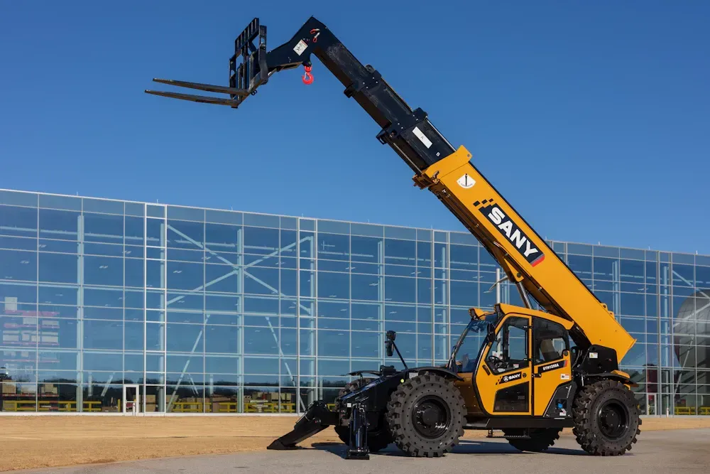 Yellow SANY telehandler with raised boom, in front of a glass building on a sunny day.