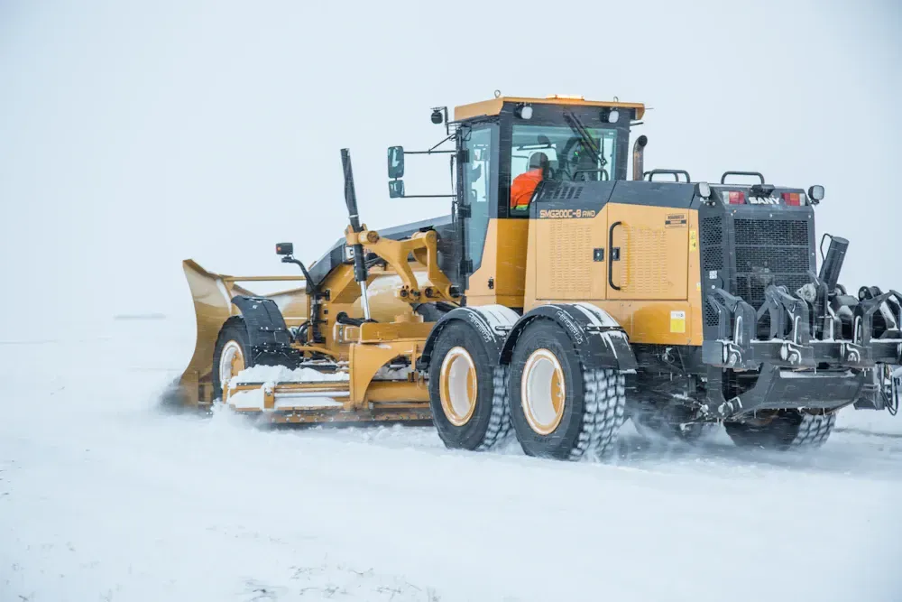 Yellow grader plowing snow on a road.