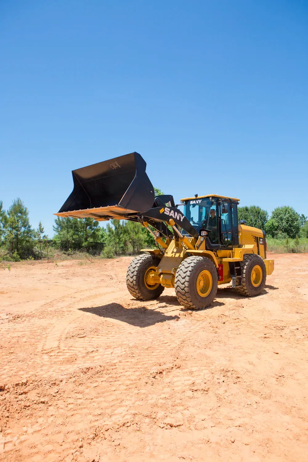 Yellow front-end loader with raised bucket on a dirt lot under a blue sky.