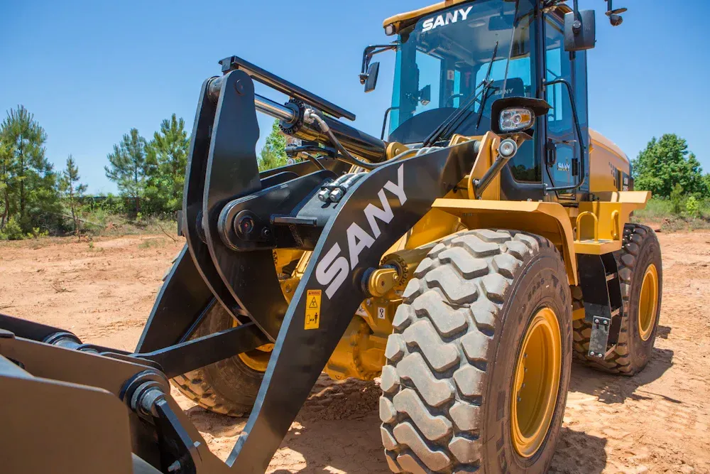 Yellow SANY wheel loader on a dirt lot, with black grapple attachment.