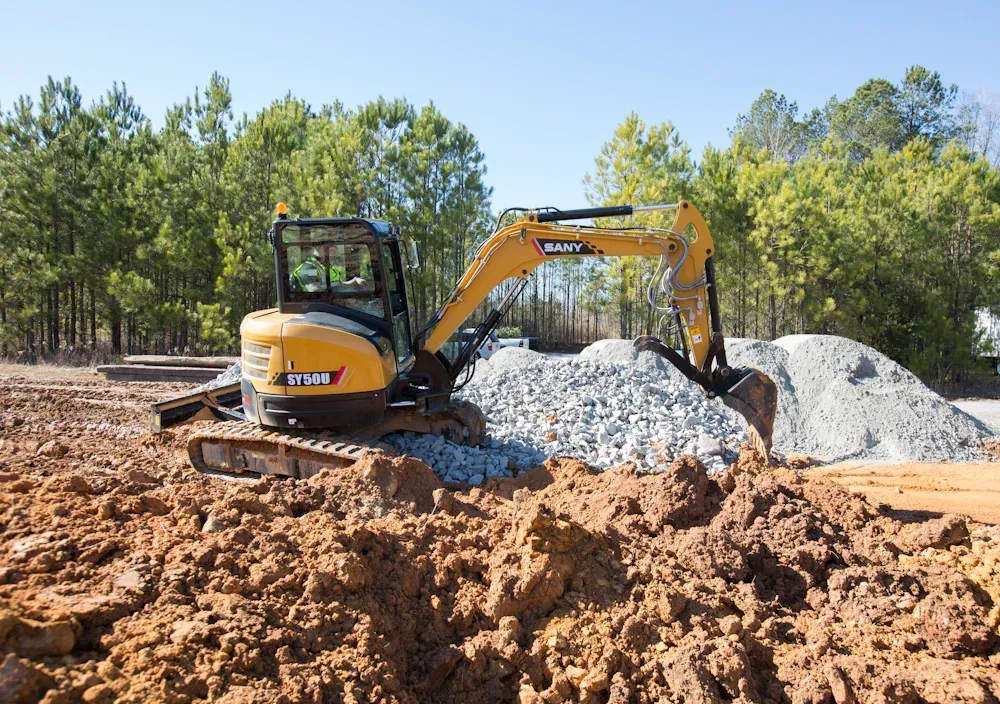 Orange and black backhoe loader with raised buckets on a paved area.