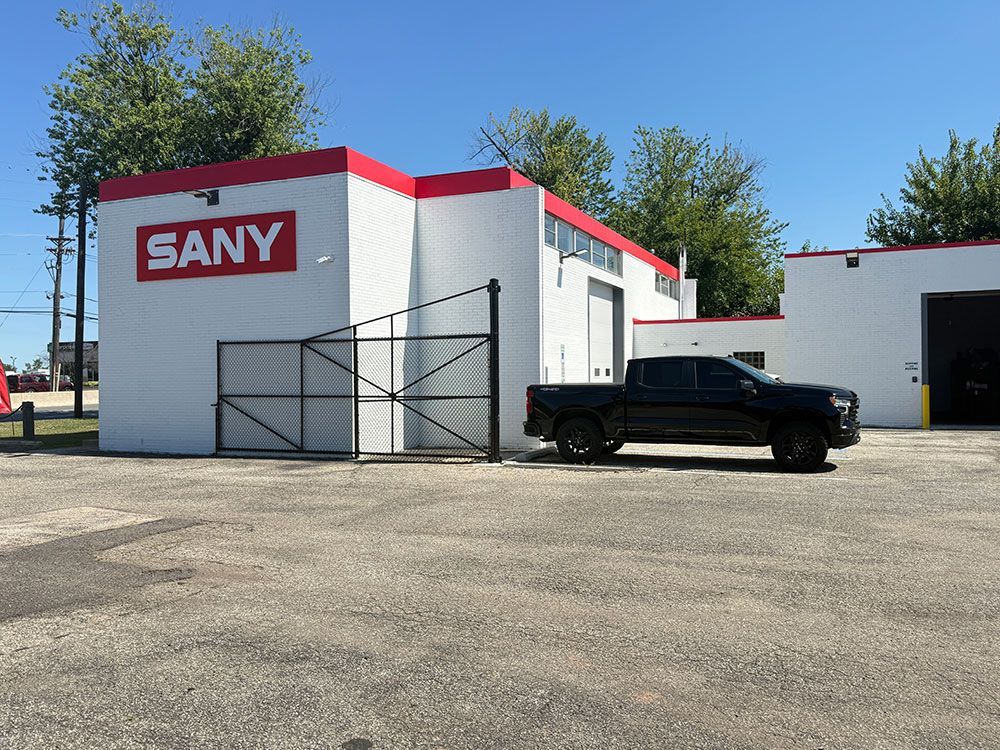 SANY building with red and white facade, black truck parked in front, blue sky.