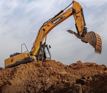 Yellow SANY excavator digging in a dirt pile under a cloudy sky.