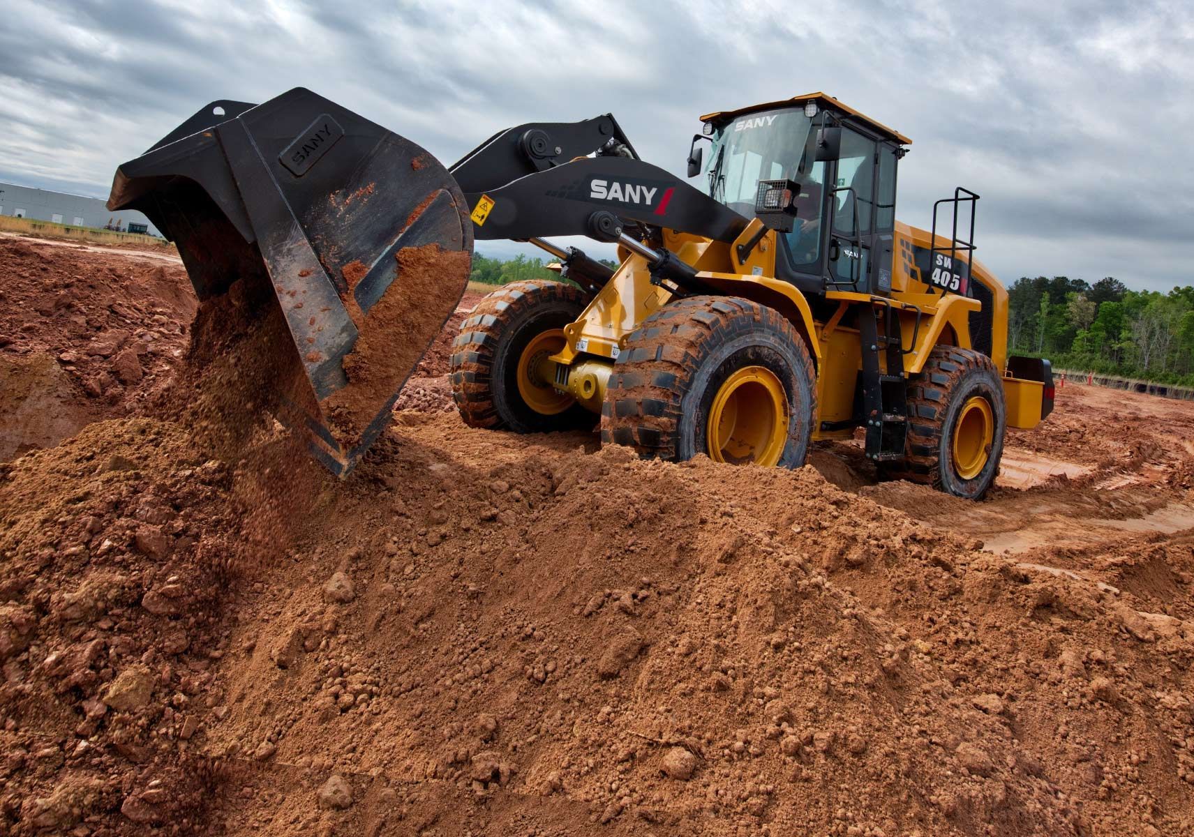 Yellow SANY wheel loader with raised bucket on a dirt surface under a blue sky.