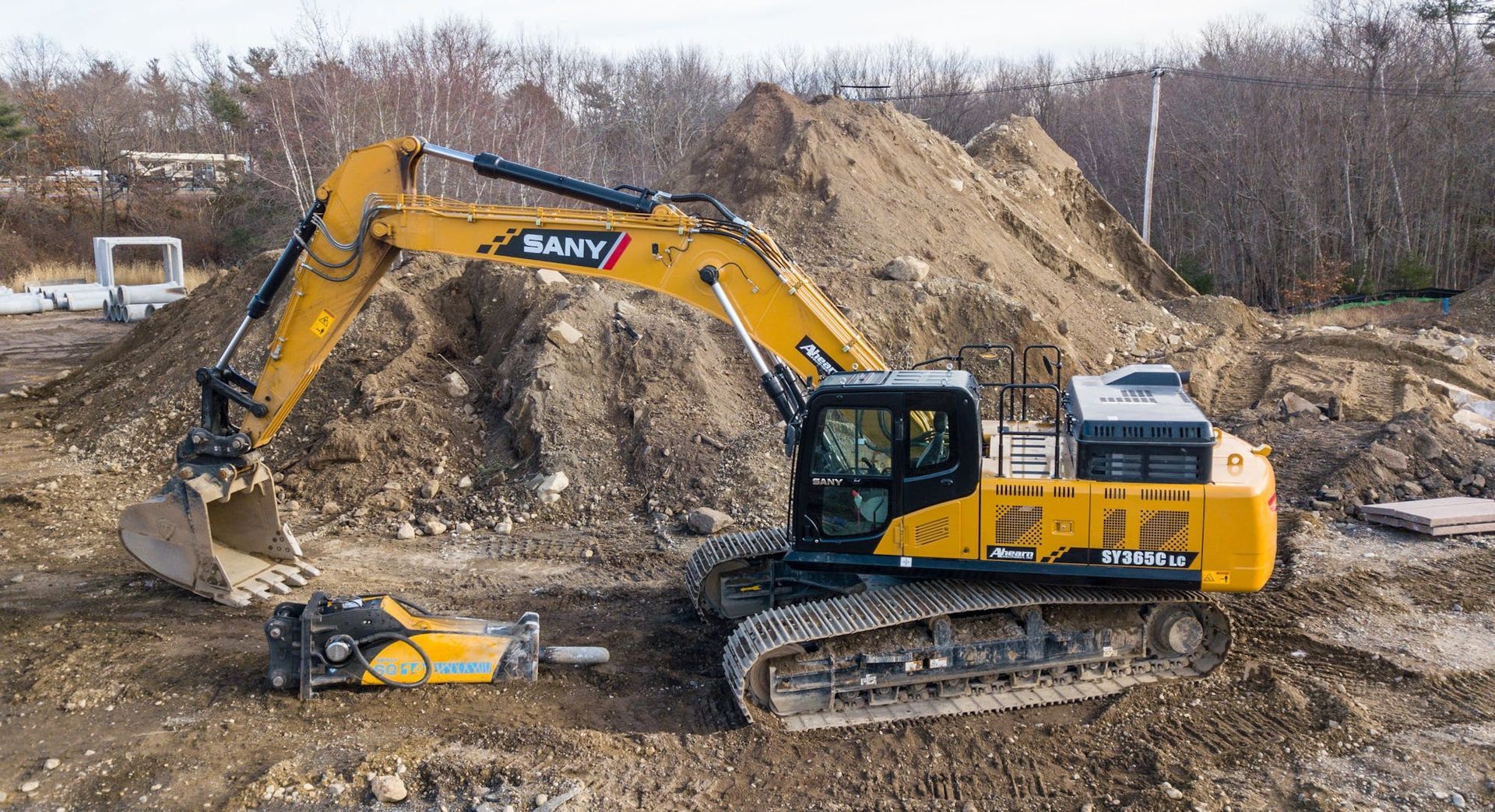 Yellow SANY excavator on a construction site, near a pile of dirt and a yellow demolition tool.