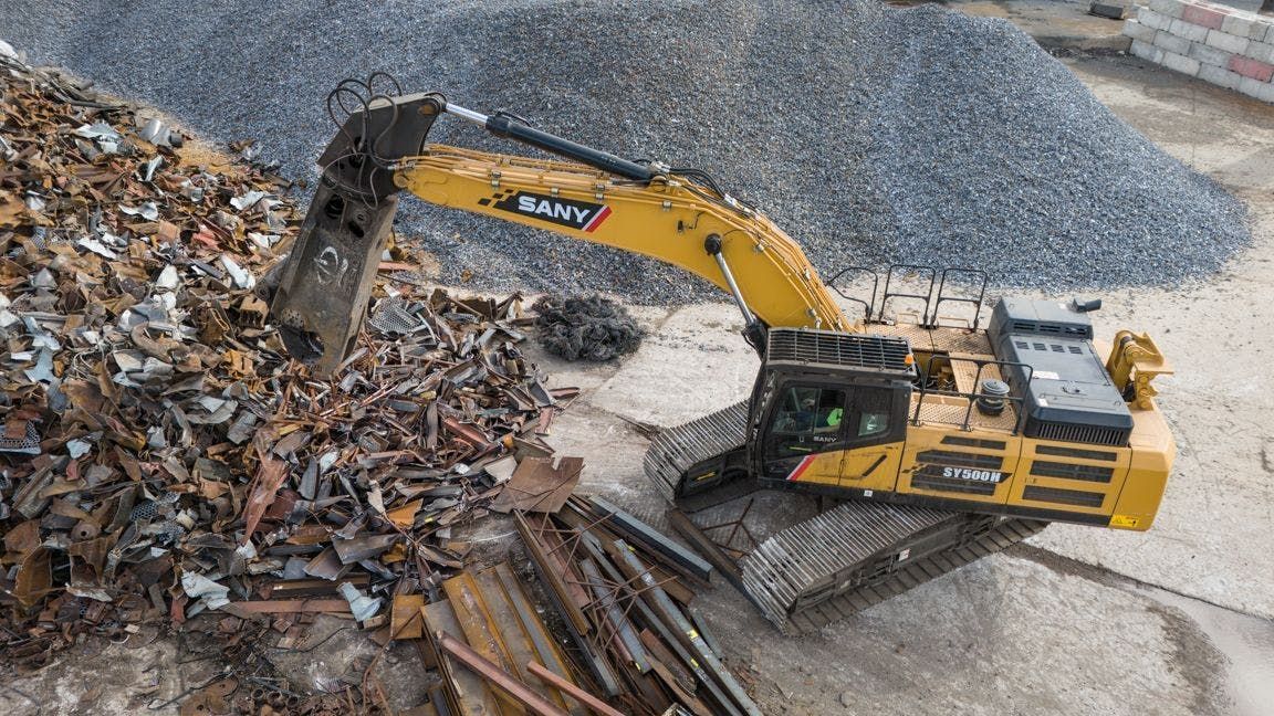 Yellow excavator sorting scrap metal at a recycling facility.