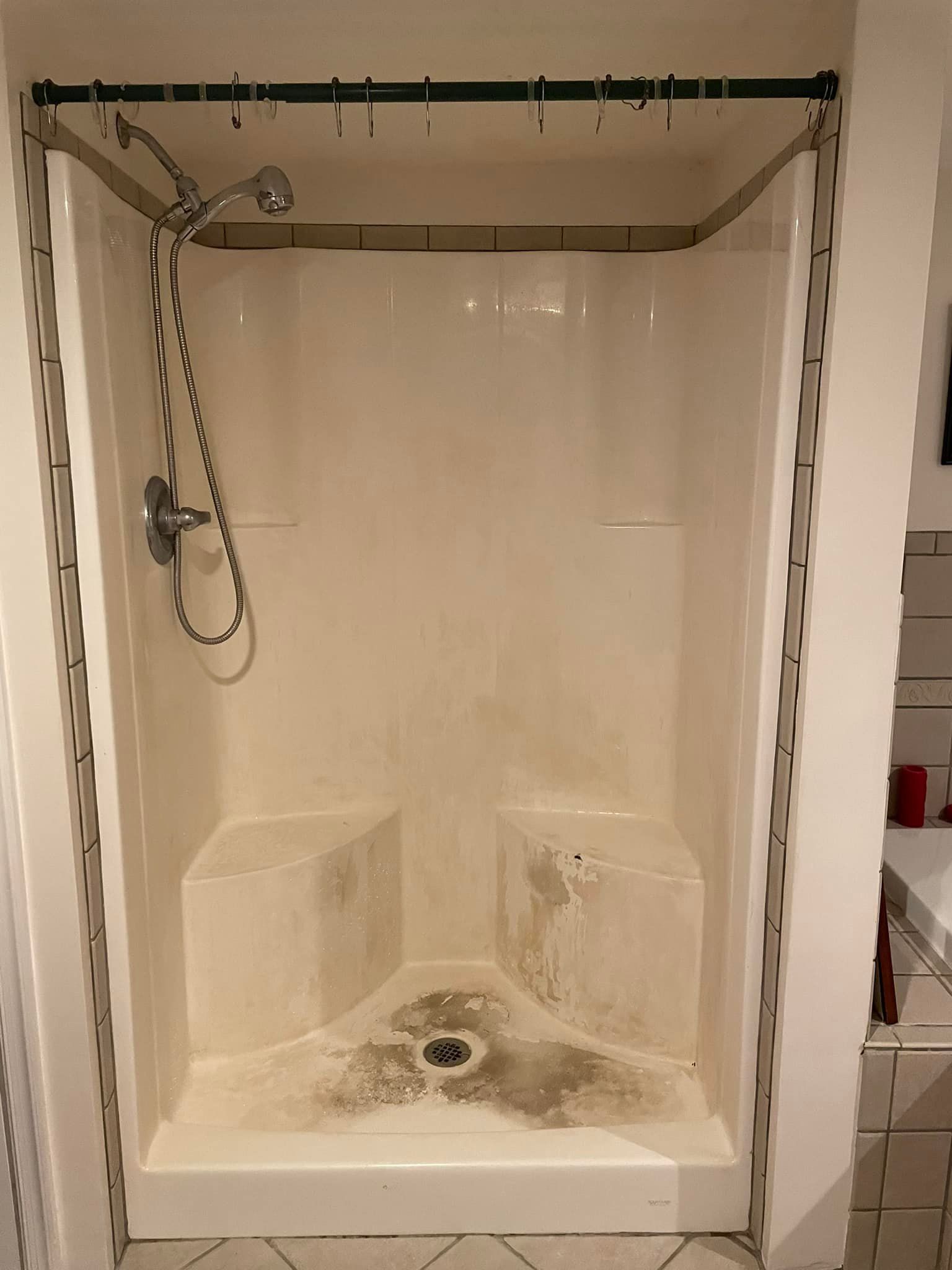 A dirty shower stall with a shower head and seats in a bathroom.