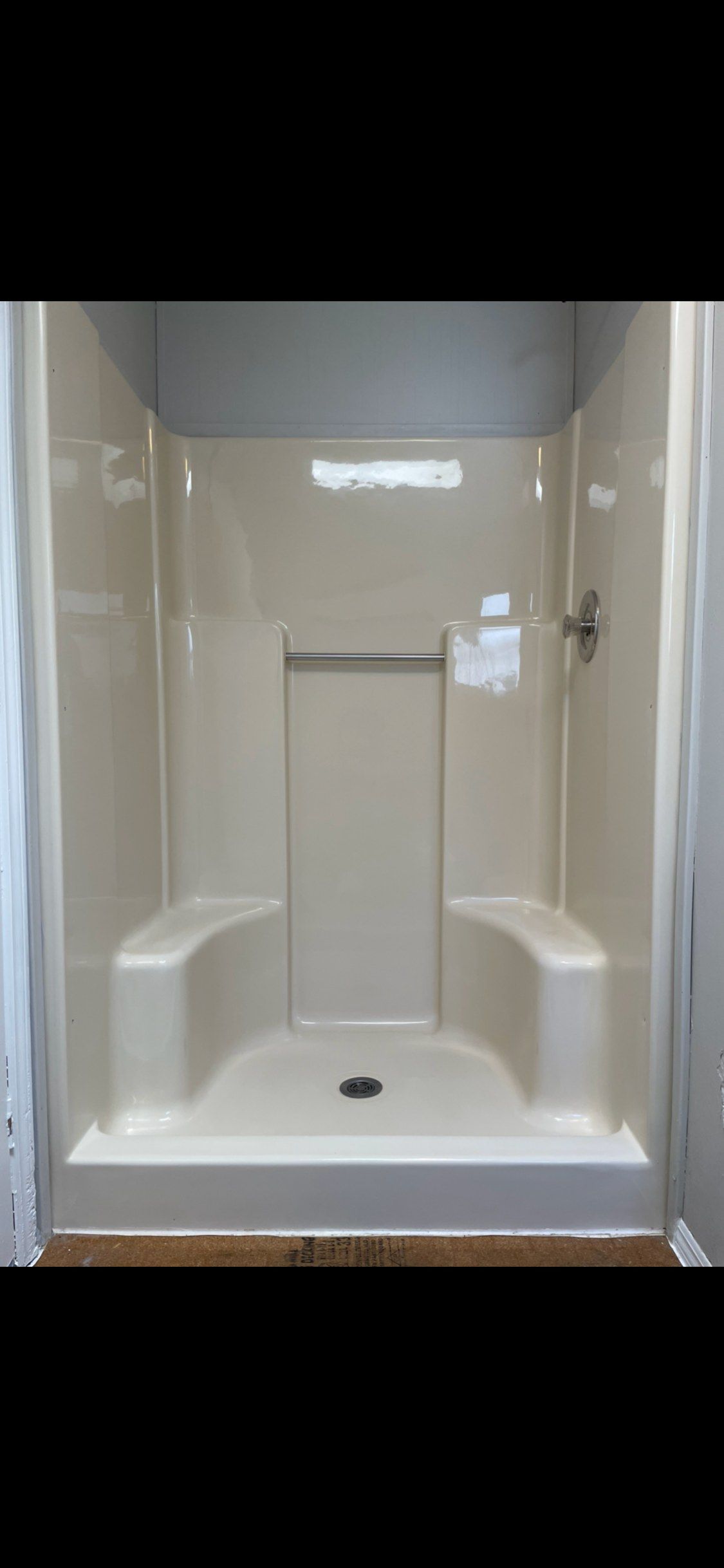 A white shower stall with two benches and a shower head.
