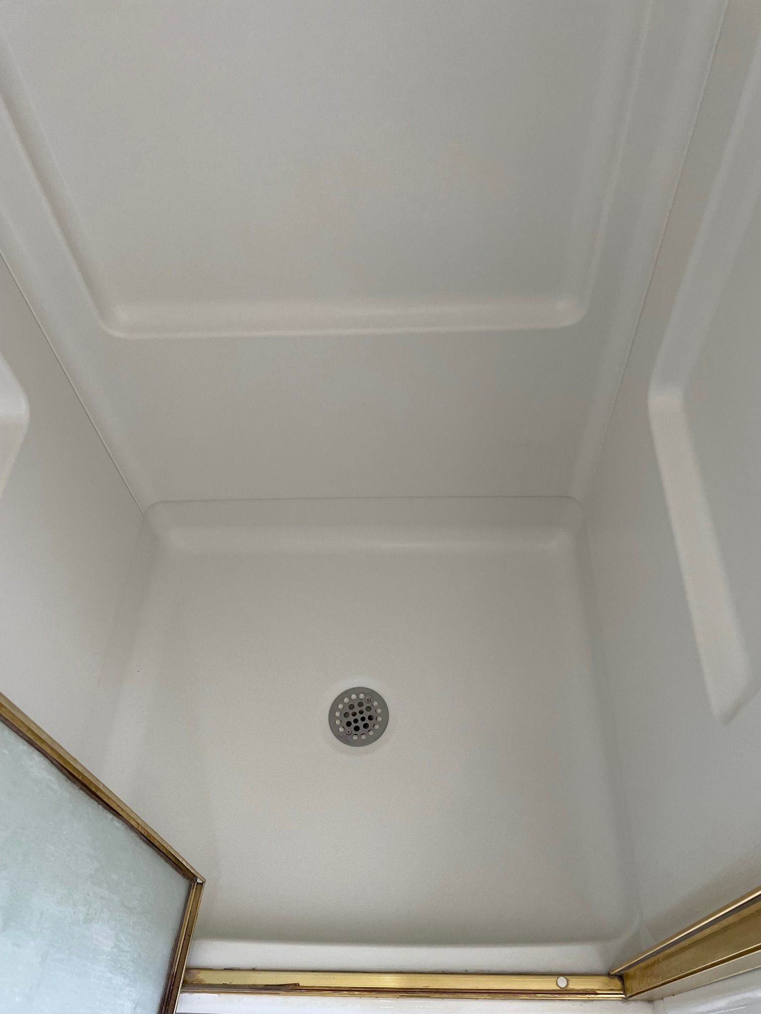 A white shower stall with a gold trim and a drain.
