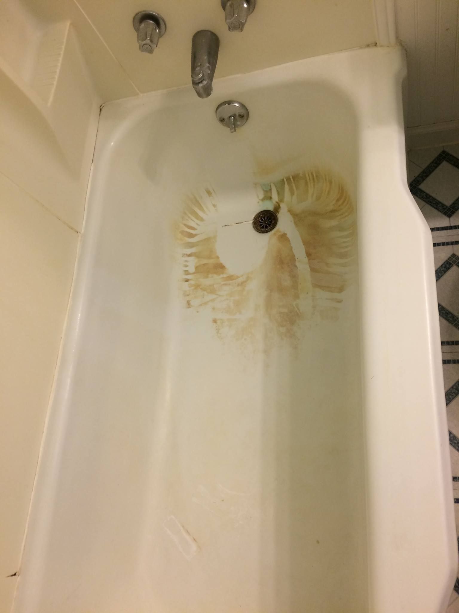 A white bathtub with a dirty drain in a bathroom.