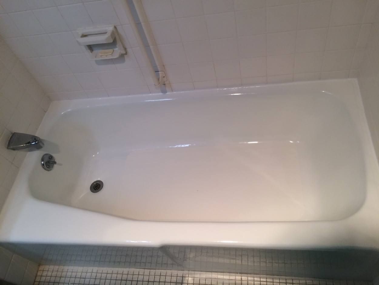White bathtub with faucet and drain, set in a tiled alcove. Soap dish visible above.