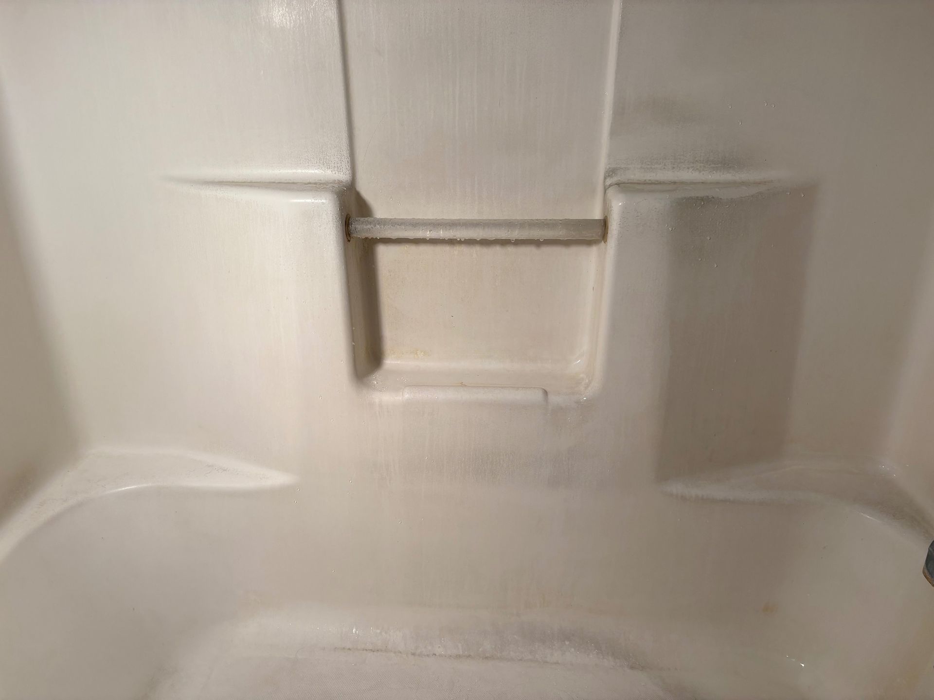 A close up of a white shower stall with a towel on the floor.