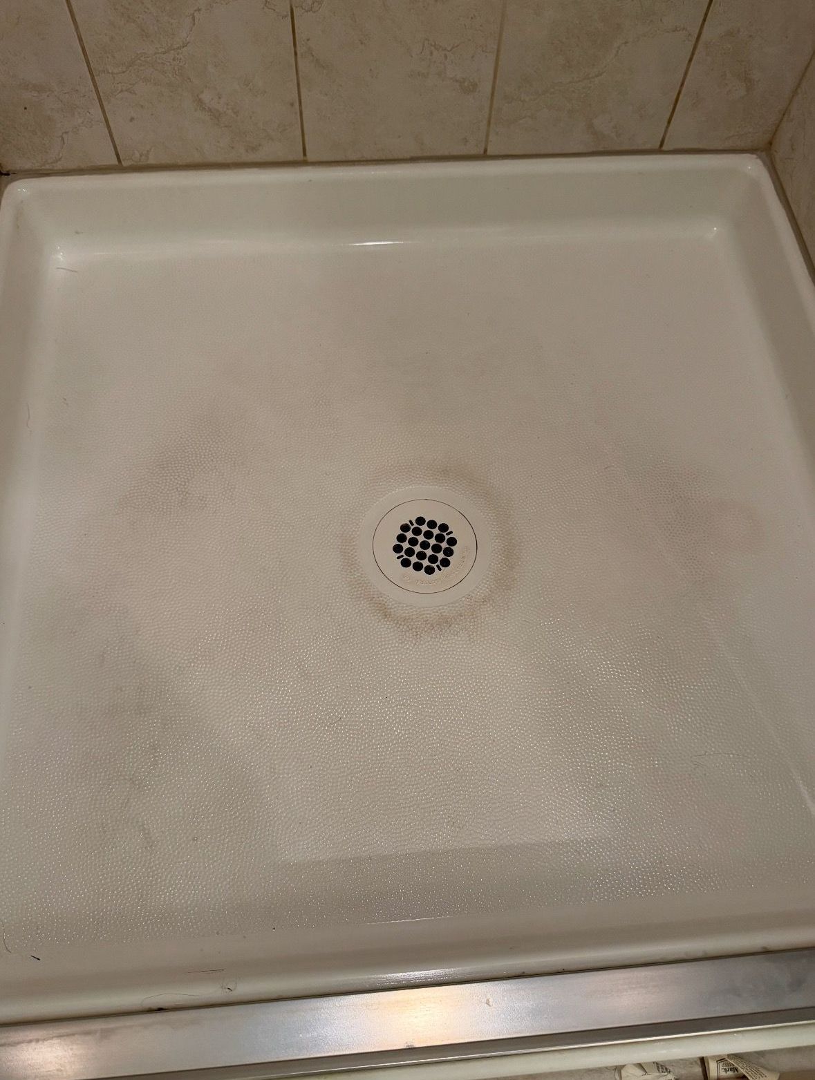 A white shower stall with a drain in the middle of it.