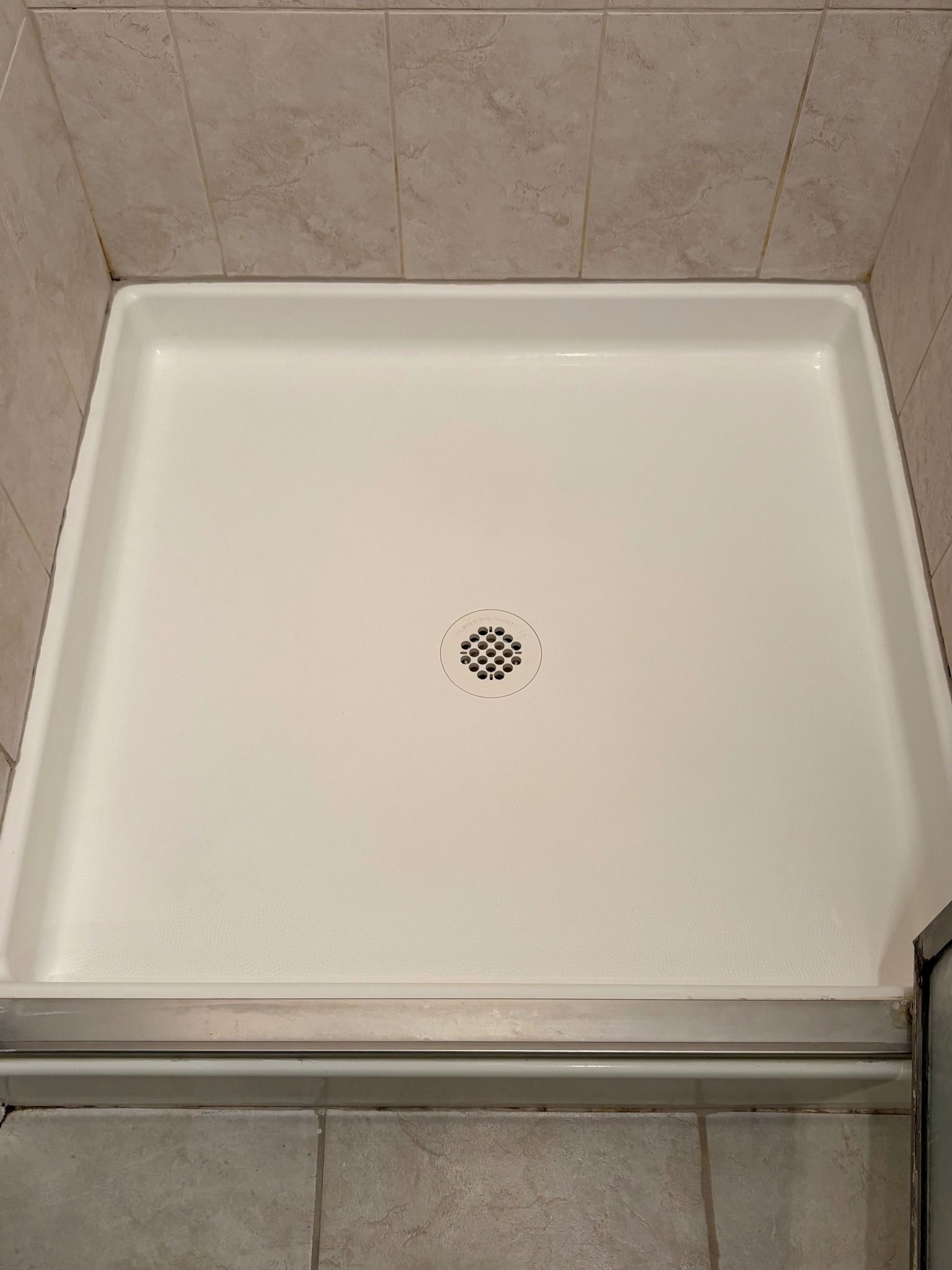 A white shower stall with a drain in a bathroom.