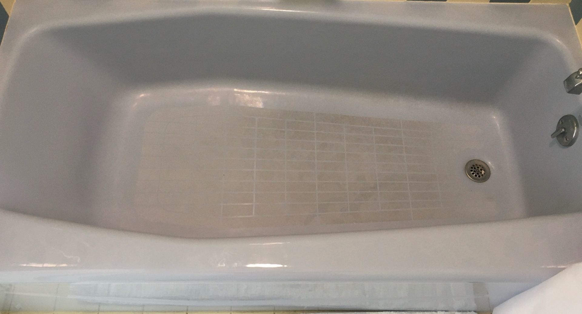 A light gray bathtub with a non-slip mat in the center, viewed from above. The faucet and drain are visible.