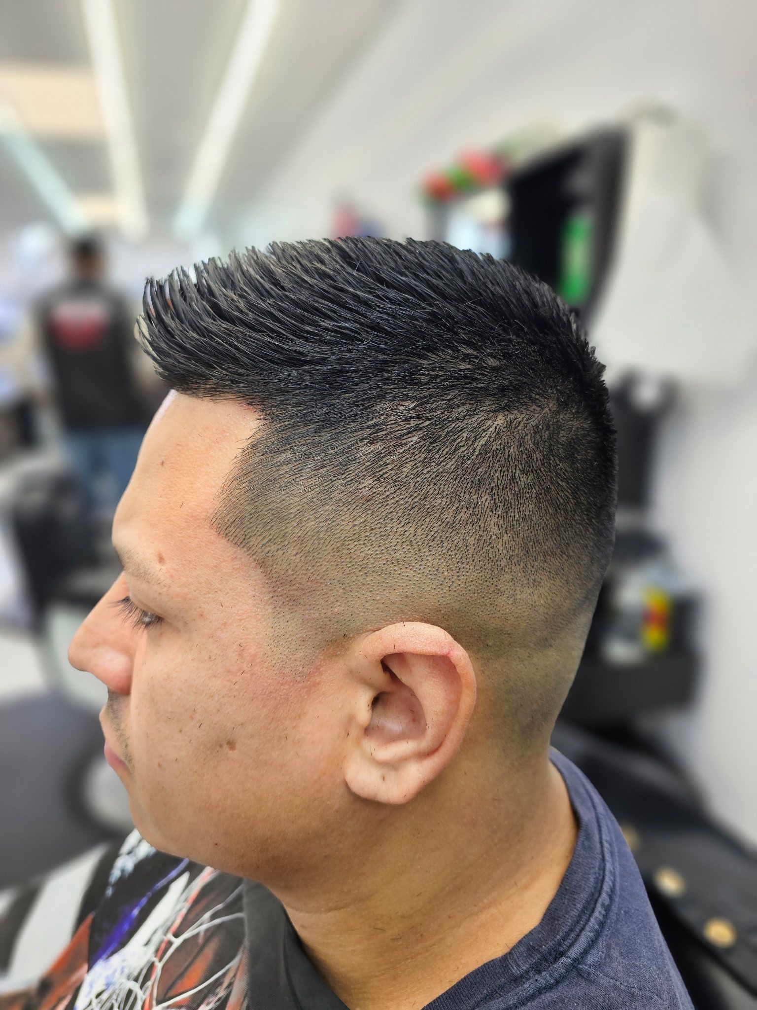 A side profile of a person with a textured, short haircut featuring a clean, precise skin fade in a barbershop.