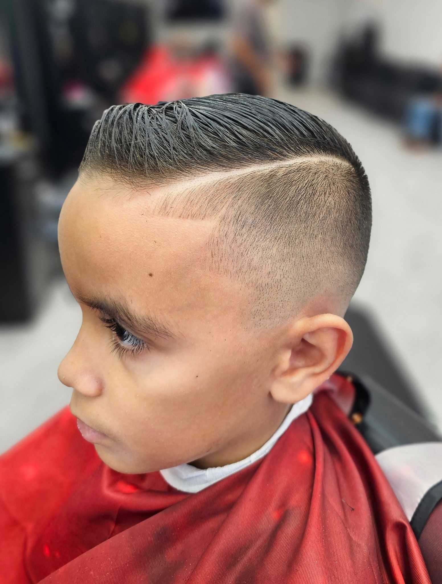 A close-up of a person with a short, faded haircut featuring a shaved line part and styled hair on top.