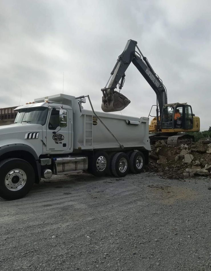 A dump truck is being loaded with dirt by an excavator.