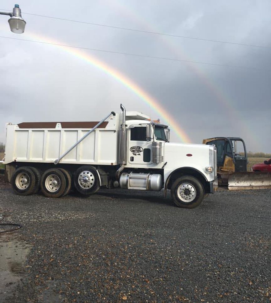 A white dump truck is parked in front of a rainbow A white dump truck is parked in front of a rainbow