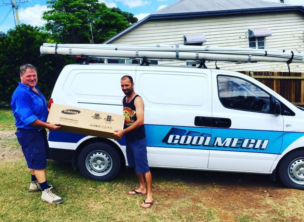 Two Men Are Standing In Front Of A Coomerb Van Holding Boxes — Coolmech In Gympie, QLD