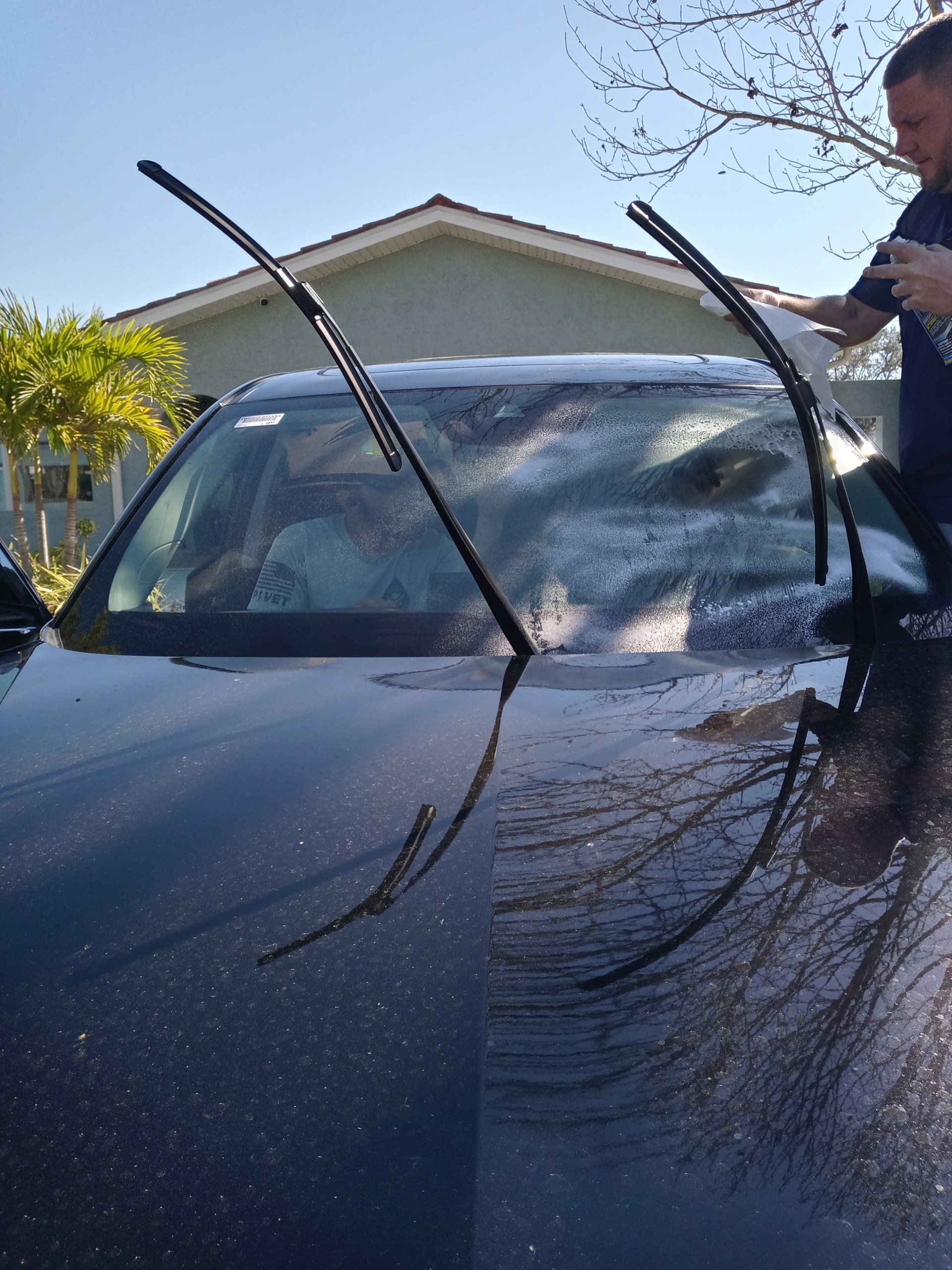 A man is cleaning the windshield of a black car