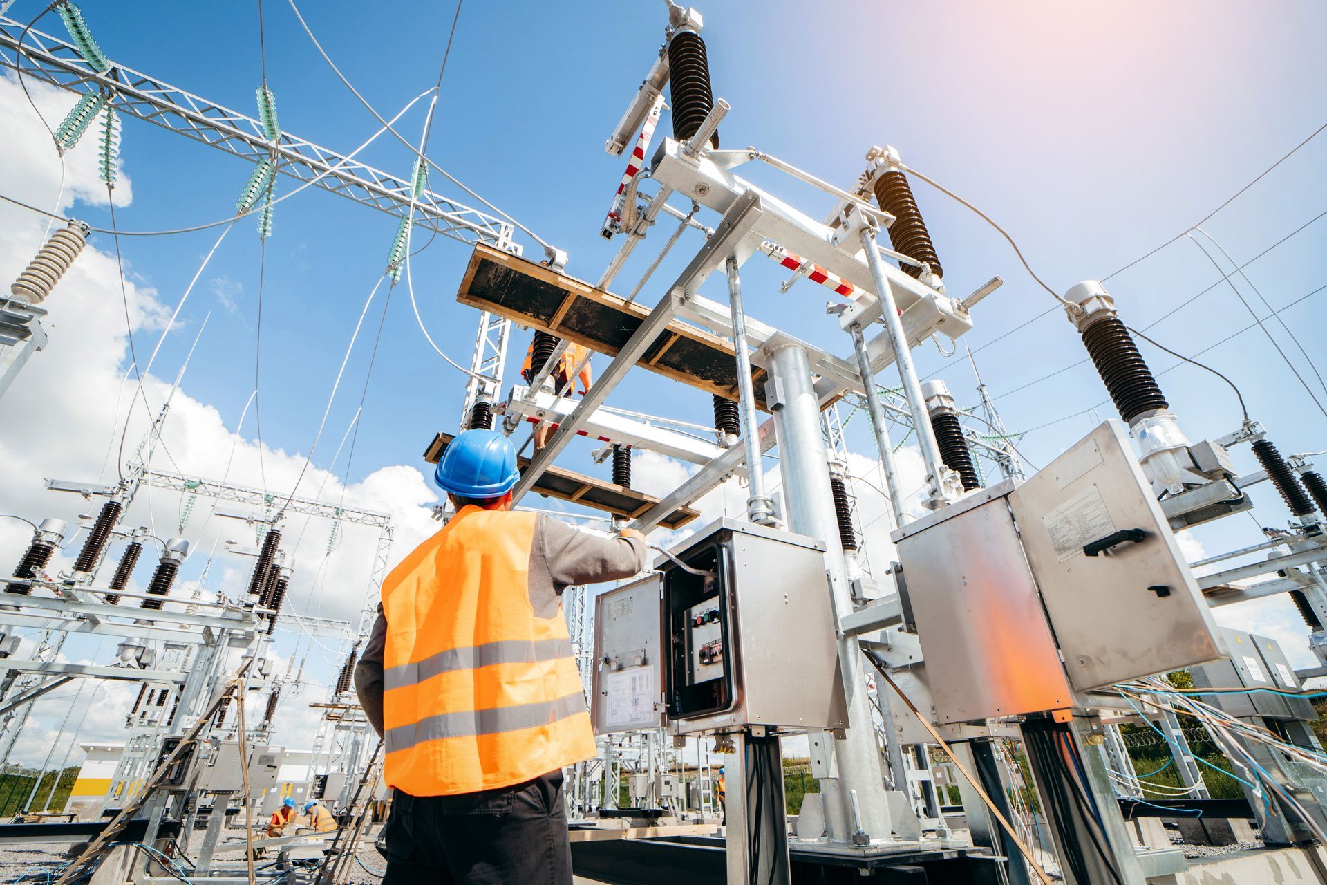 A man in an orange vest and blue helmet is working on a power station.
