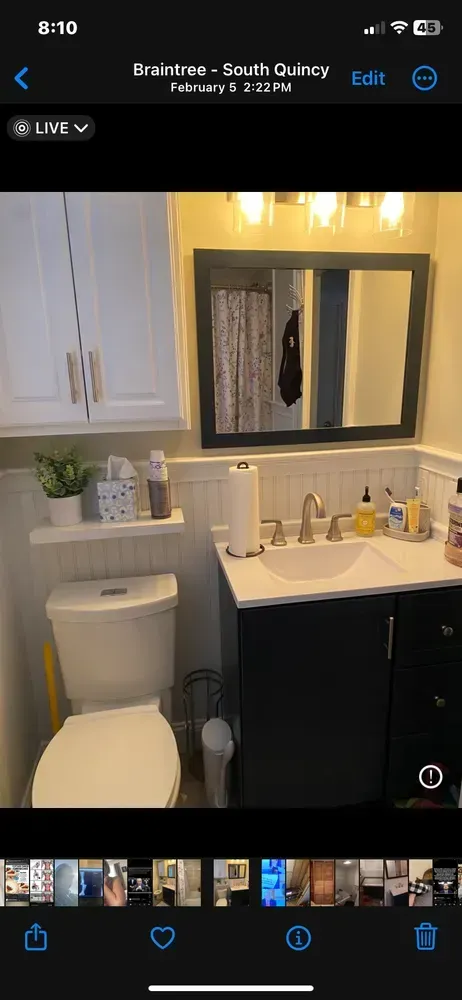 Small bathroom vanity with mirror, white sink, toilet, and black cabinet under warm lights