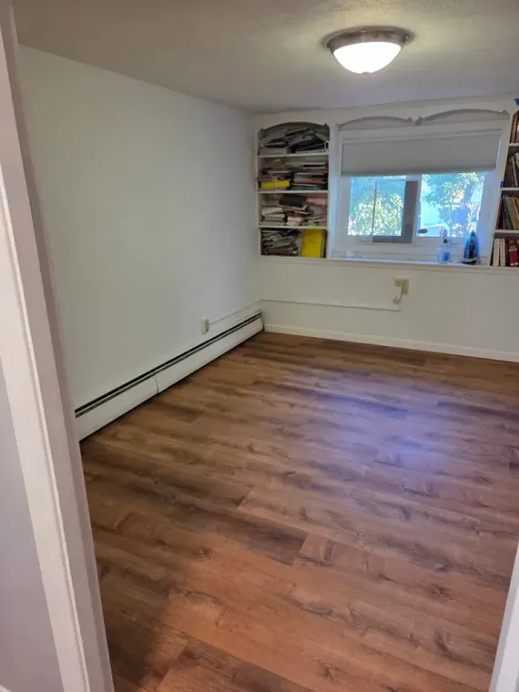 Empty bedroom with wood flooring, white walls, a window, and a built-in shelf/closet.