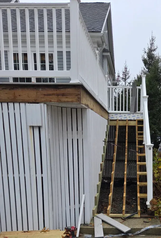 Backyard deck with white railings and stairs beside a slatted fence and retaining wall