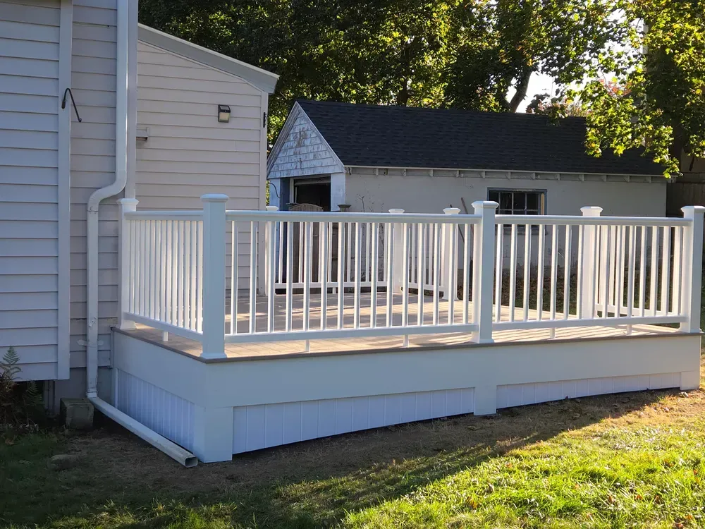White wooden deck attached to a house, with railing and steps, in a sunny yard