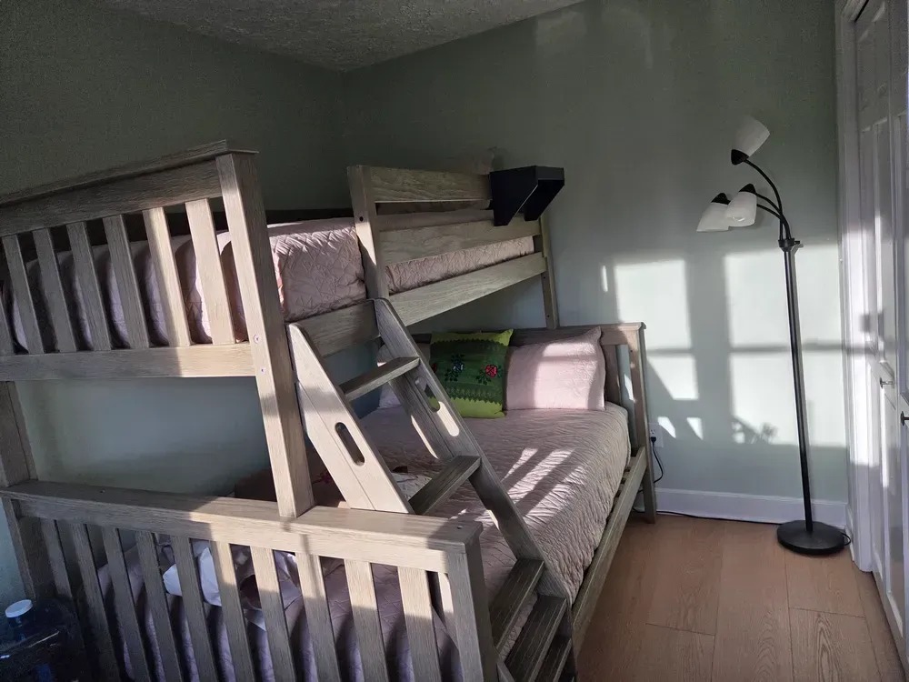 Bunk bed and floor lamp in a sunlit bedroom with pale green walls and hardwood floor