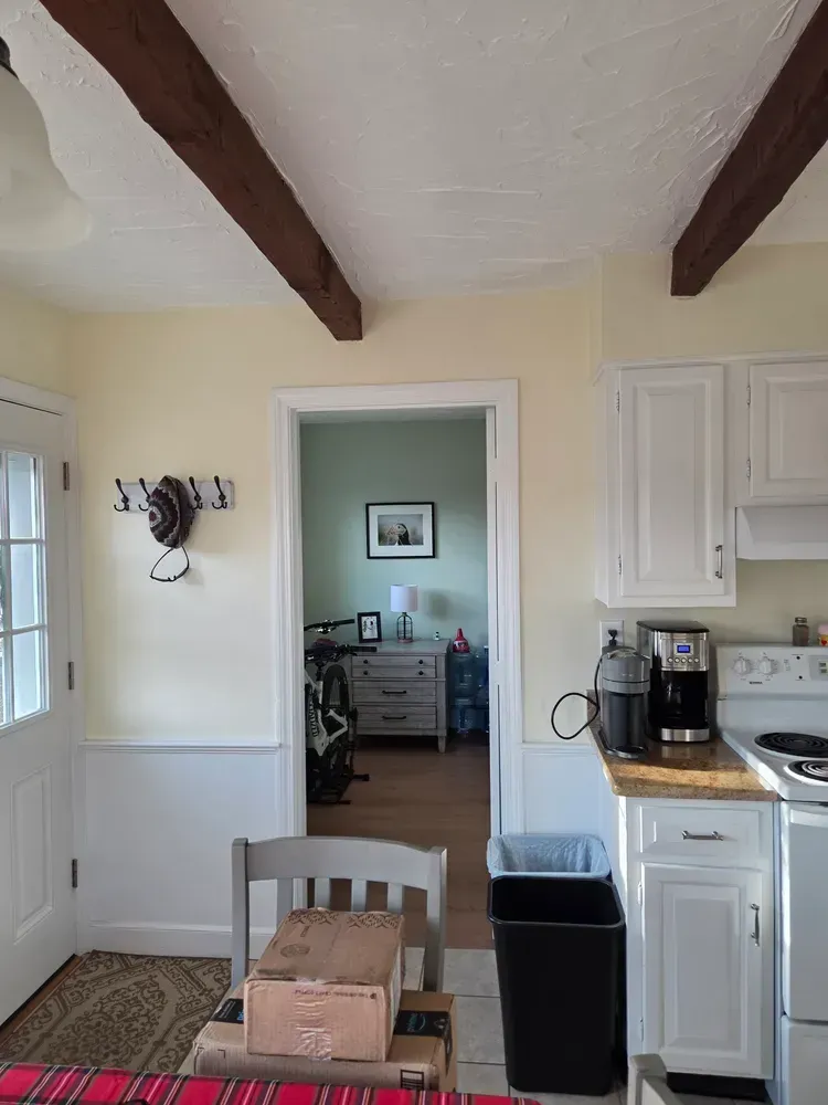 Kitchen with white cabinets, exposed beams, and doorway to a home office in back.