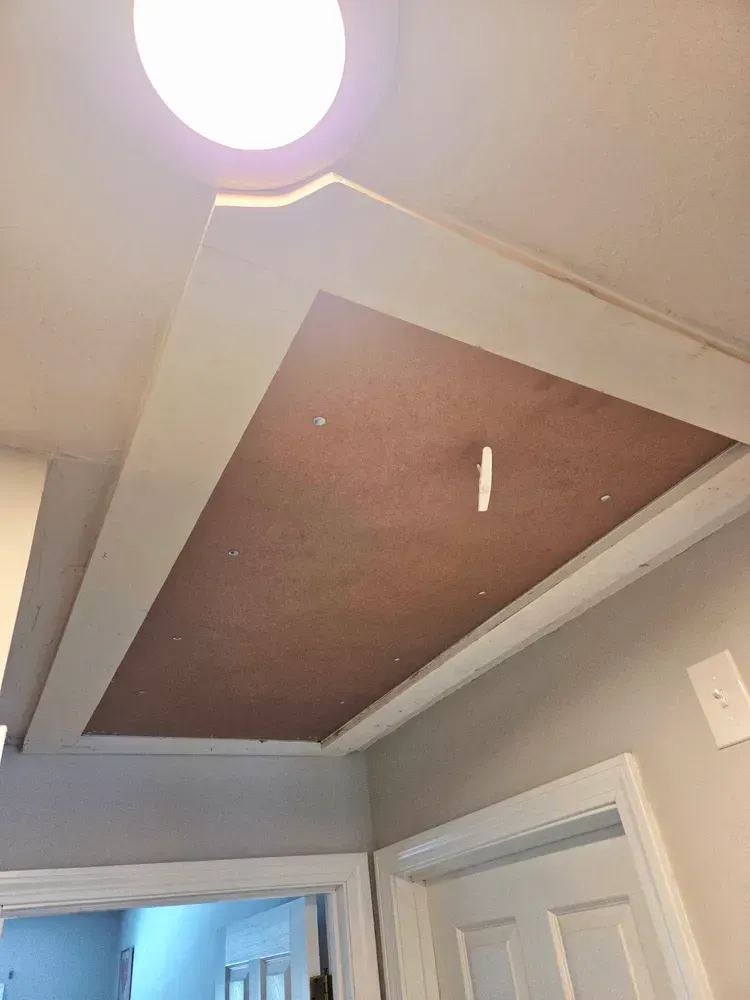 Brown attic hatch in white ceiling above a doorway, with a round ceiling light nearby.