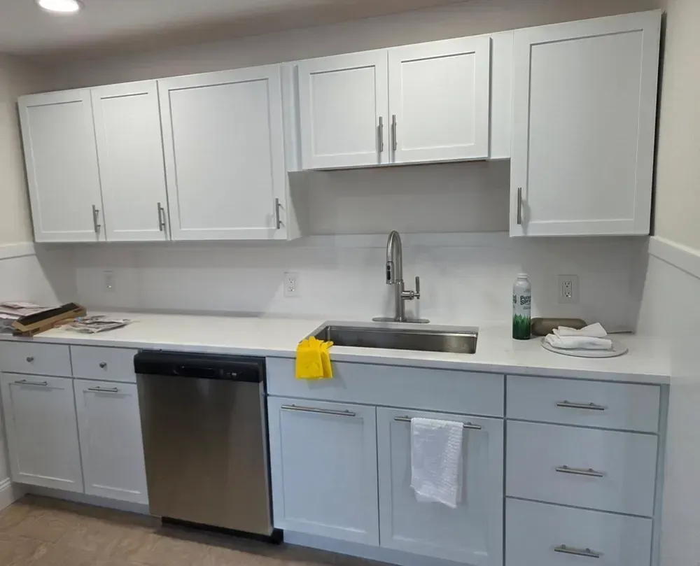 Empty bedroom with wood flooring, white walls, built-in shelves, and a window with blinds