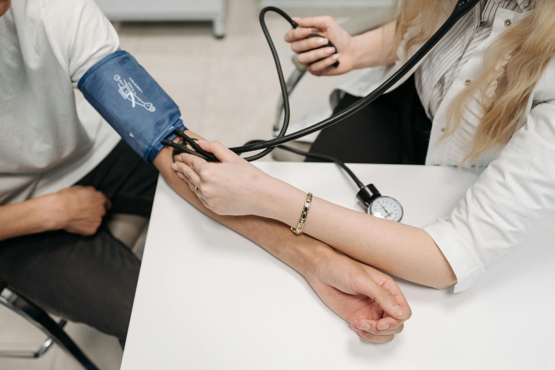 Person having blood pressure taken by a doctor with a stethoscope in a medical setting.