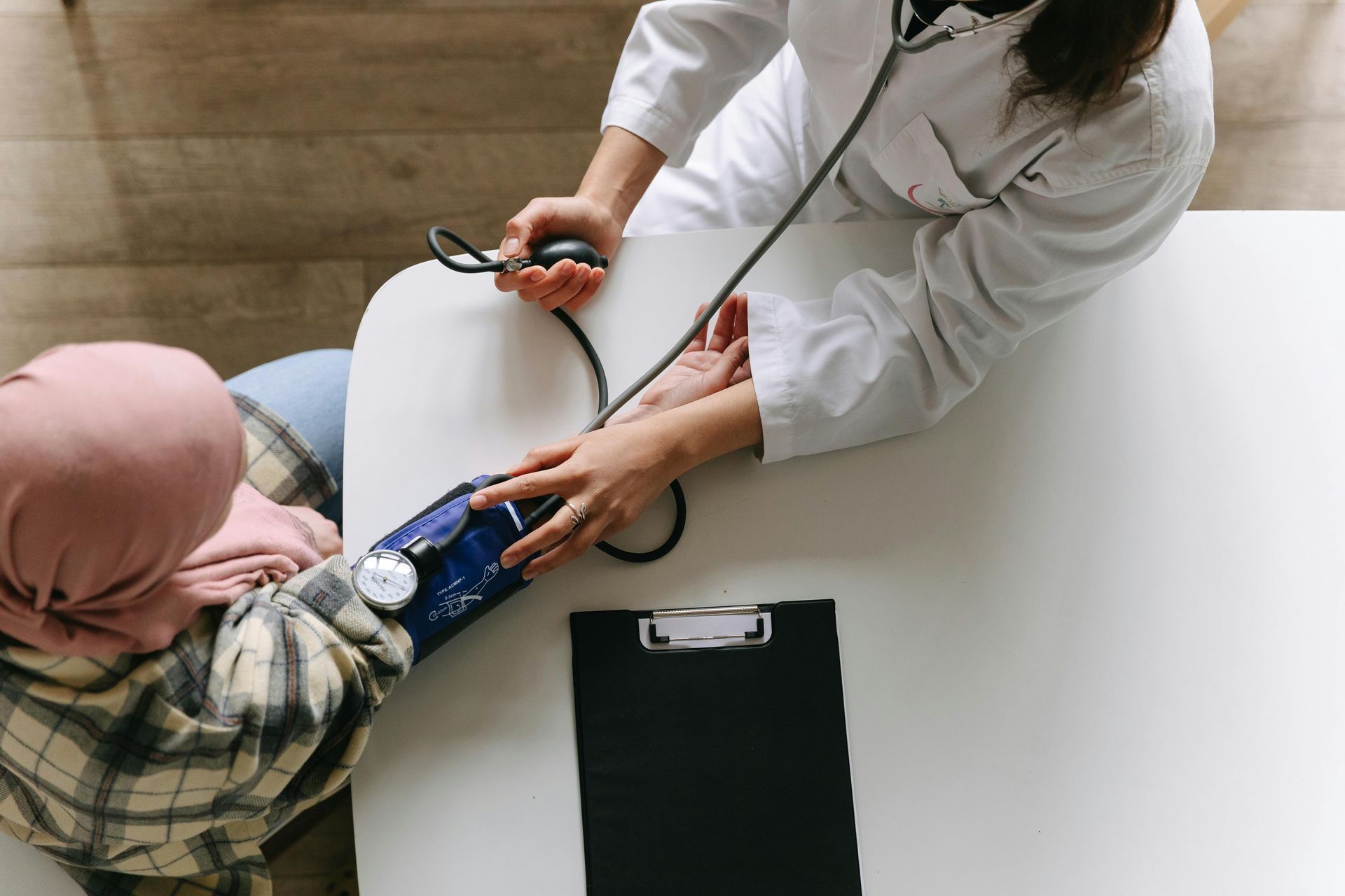 Doctor taking patient's blood pressure with a stethoscope and cuff at a white table.